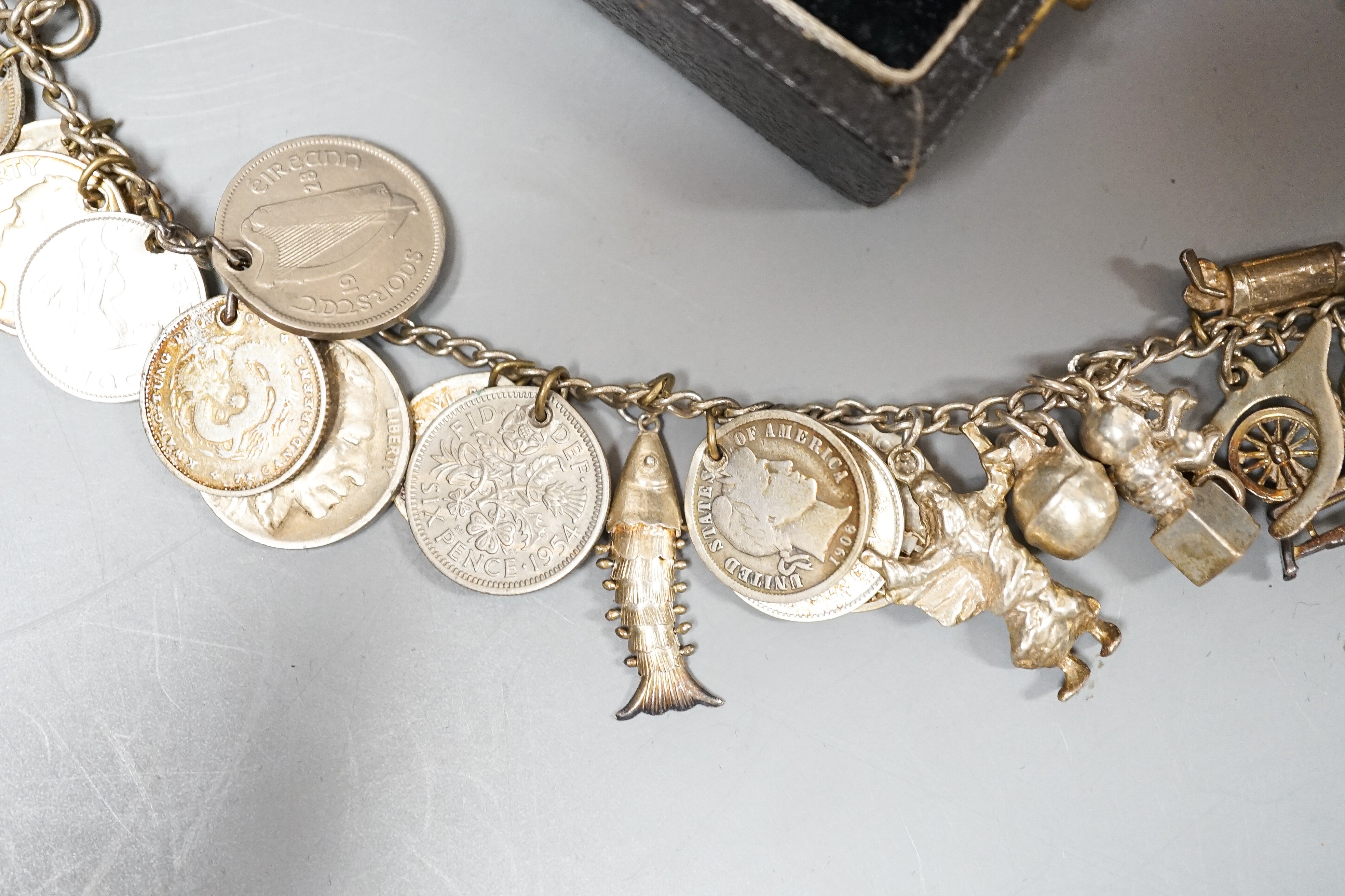 A 1930's cased silver christening set, comprising an egg cup, spoon and napkin ring, together with a white metal charm bracelet hung with assorted charms and coins including silver.